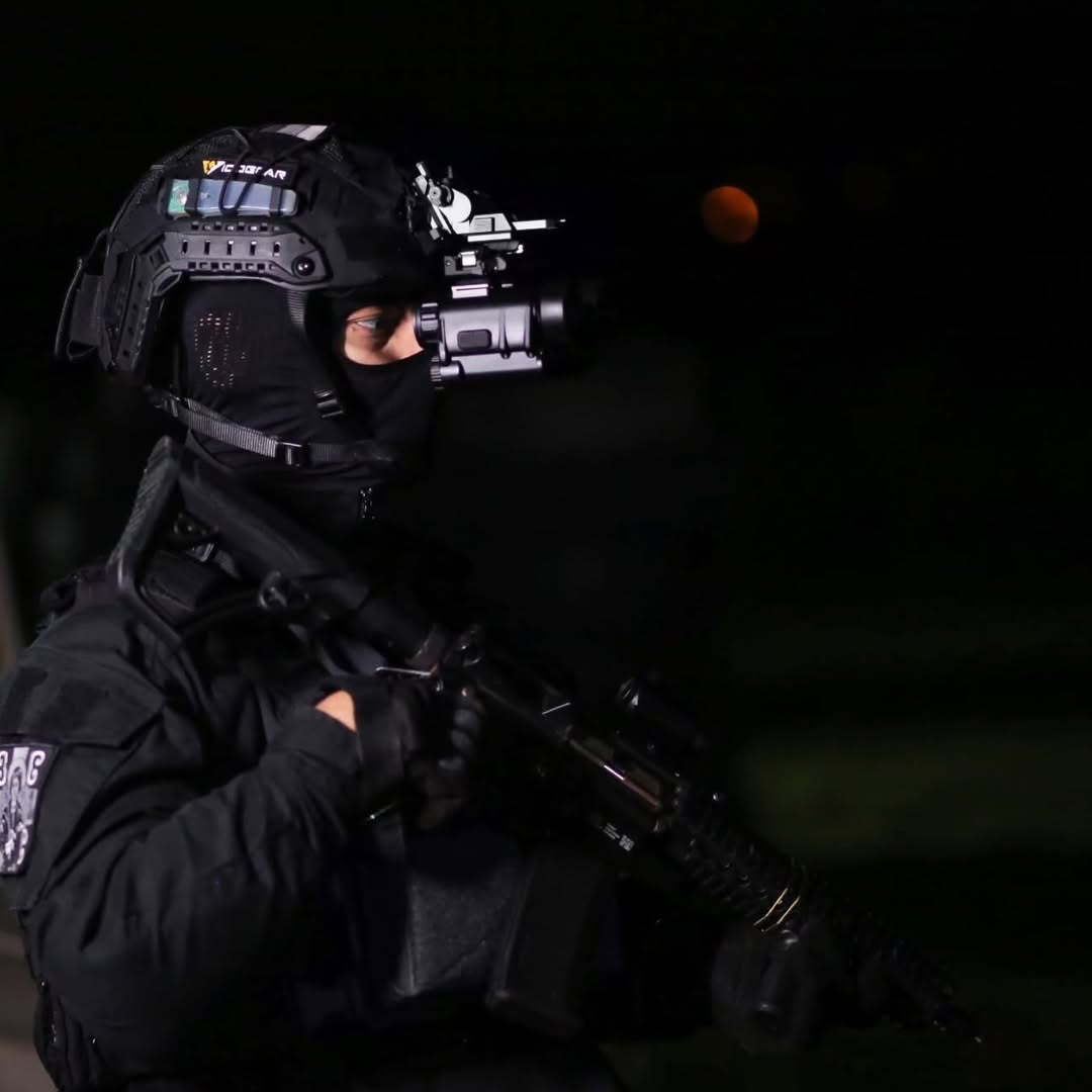 Person in tactical gear holding a rifle and night vision device NVG30 with a dark background